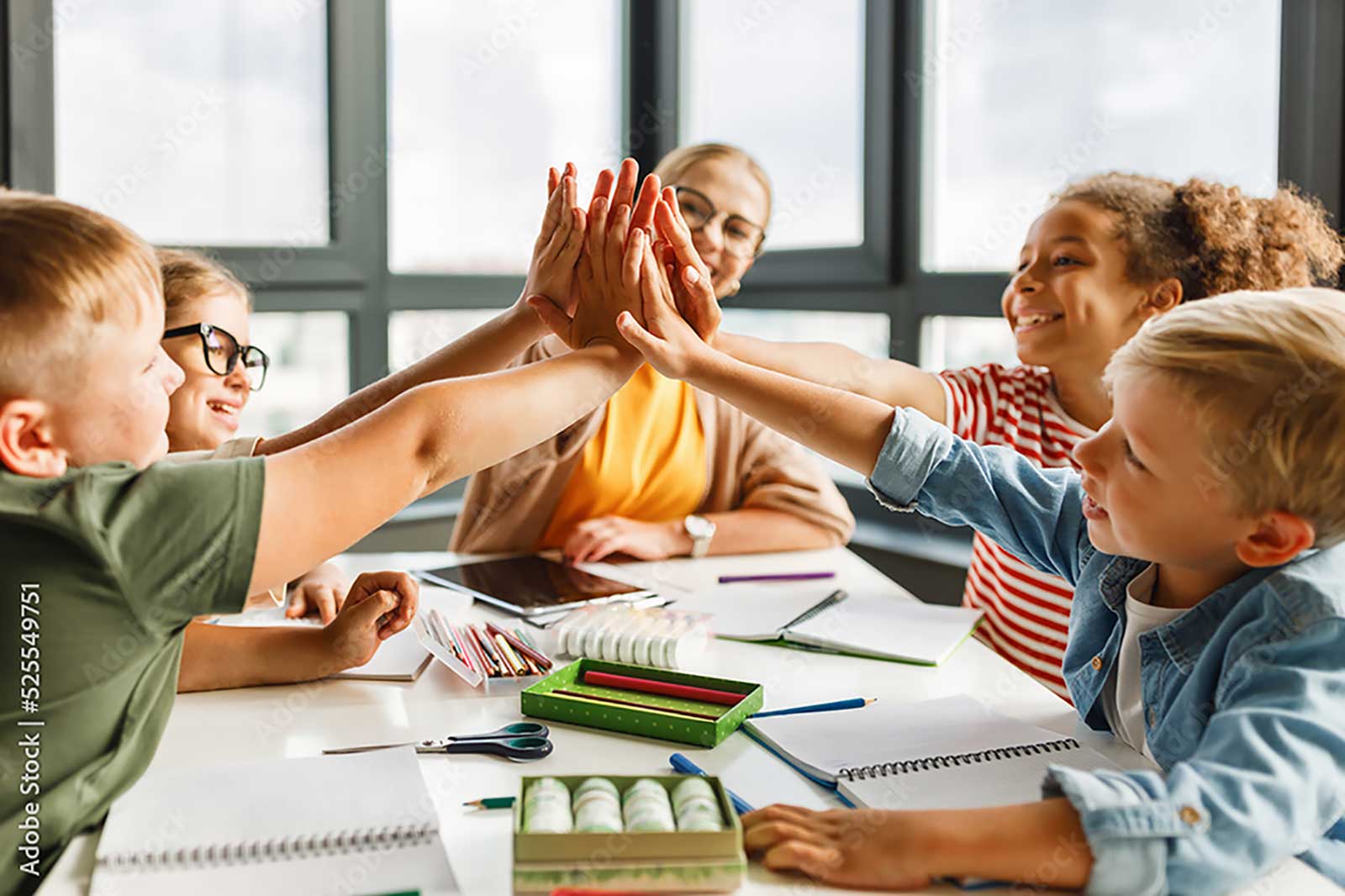 Sechs Hände treffen sich in einem Team-Hoch-Five über einem Tisch mit Schreibmaterialien und Notizbüchern.