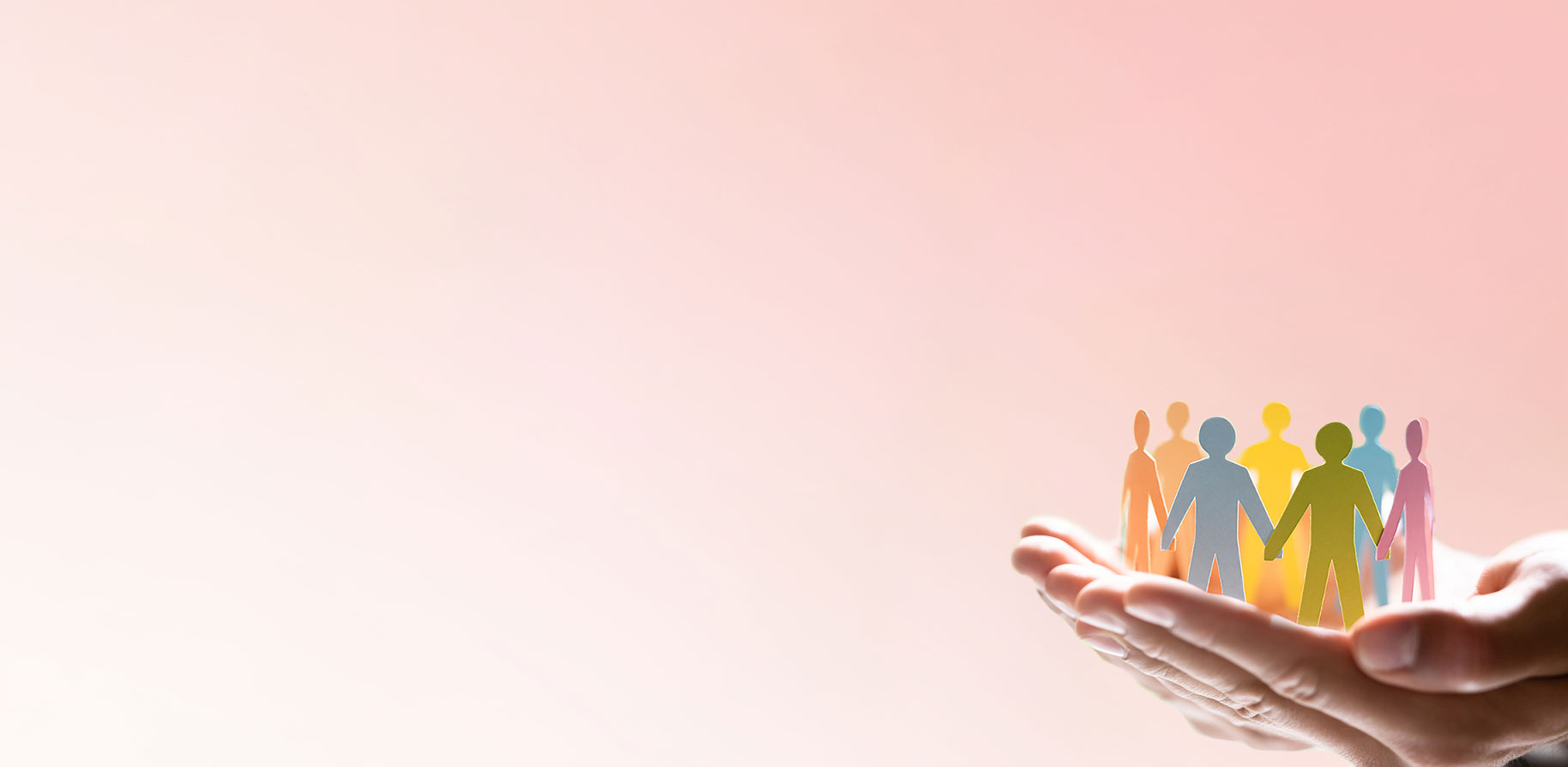 Zwei Hände halten bunte Papierfiguren, die Menschen darstellen. Der Hintergrund ist sanft rosa.