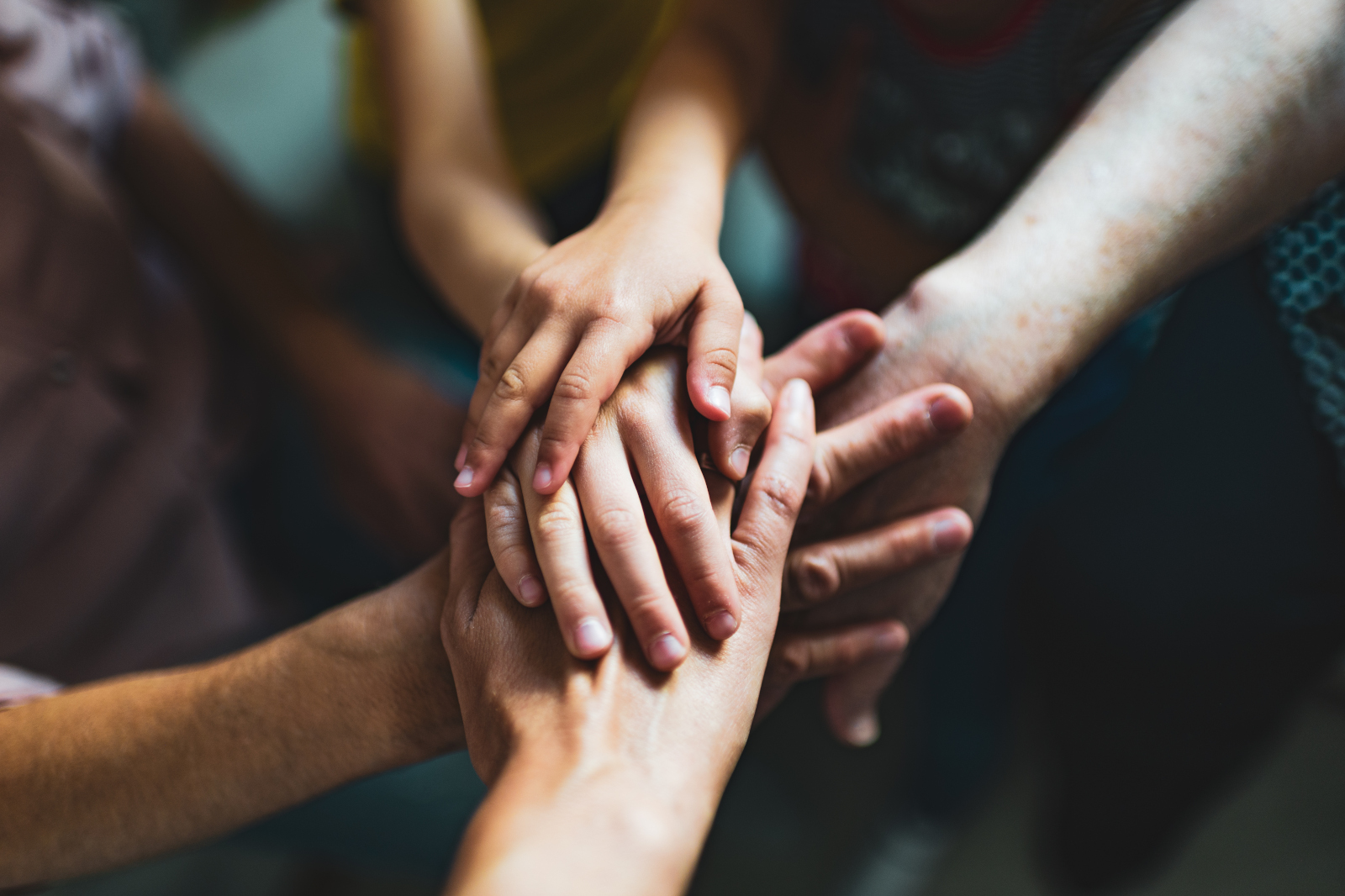 Eine Gruppe von Händen, darunter Kinderhände, liegt übereinander, was Gemeinschaft und Zusammenarbeit symbolisiert.
